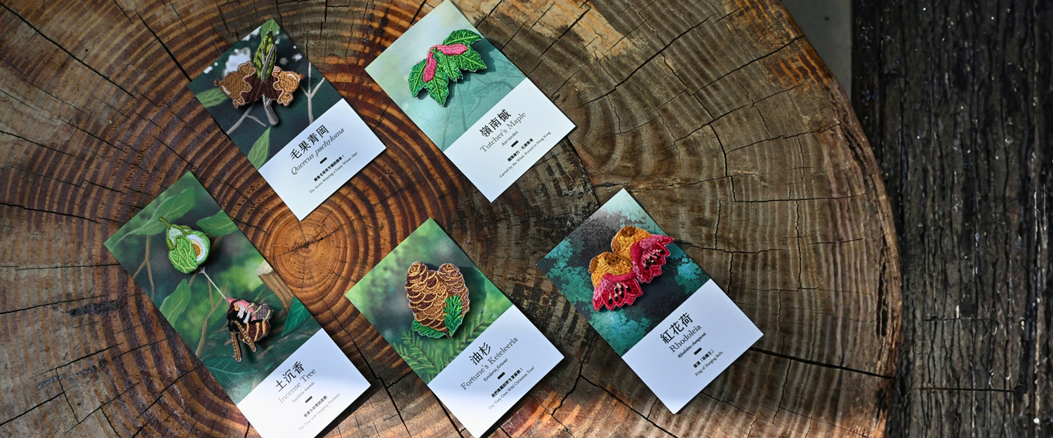 All five designs laid out on a cut tree stump, each embroidered pin mounted on its own illustrated backing card
