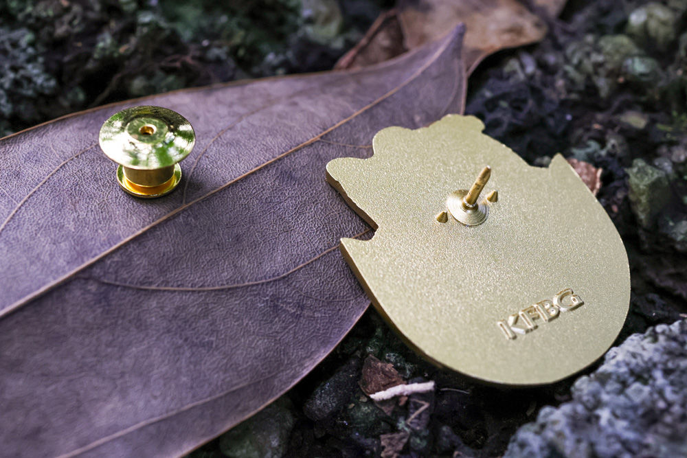 The back of a pin showing the KFBG mark and the locking pin back, laid on a dry leaf
