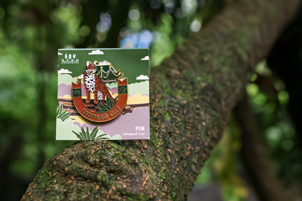 The Leopard Cat pin on its illustrated backing card, propped on a mossy tree branch