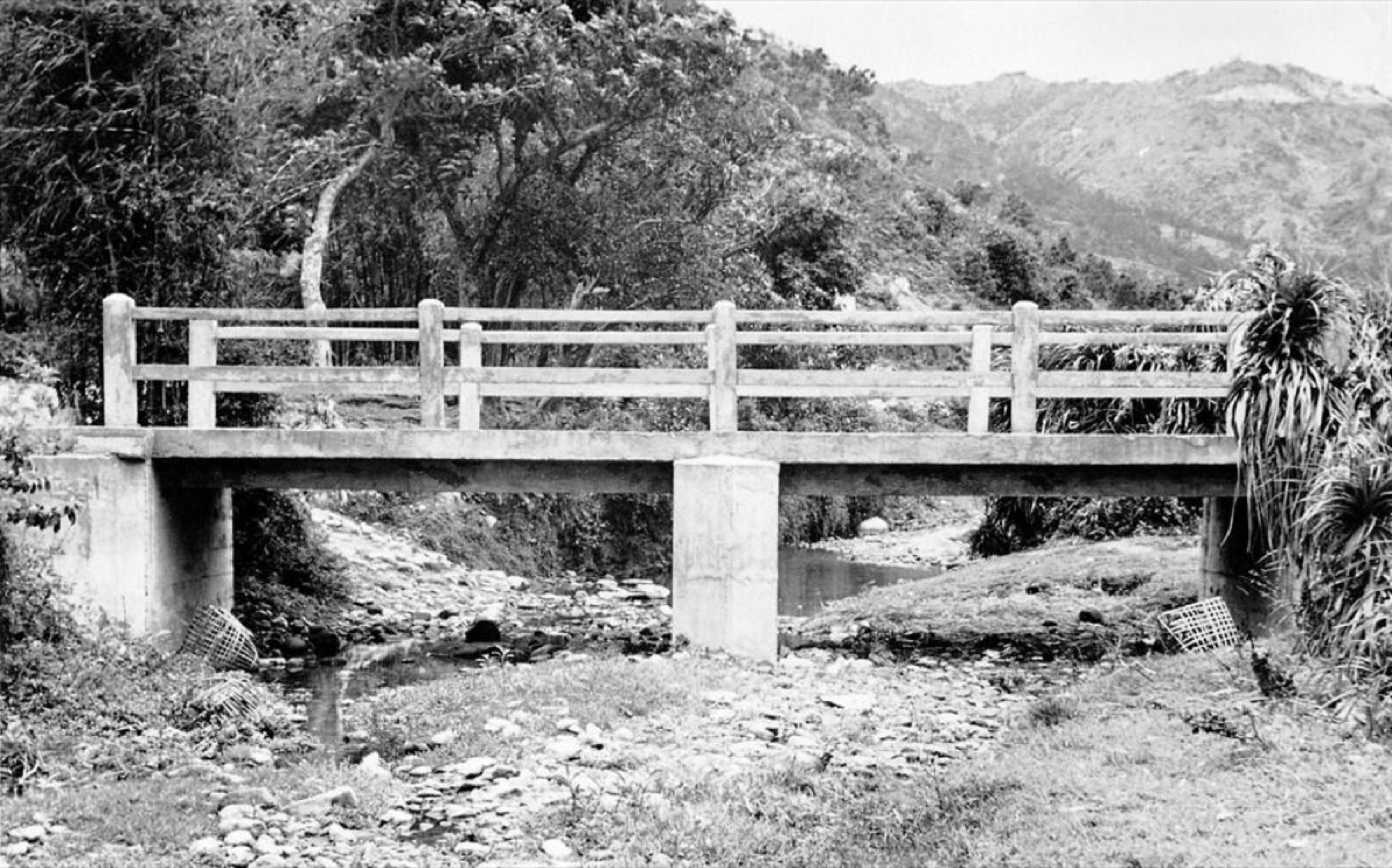 早年鄉村的混凝土行人橋橫跨溪澗，遠處為連綿山巒